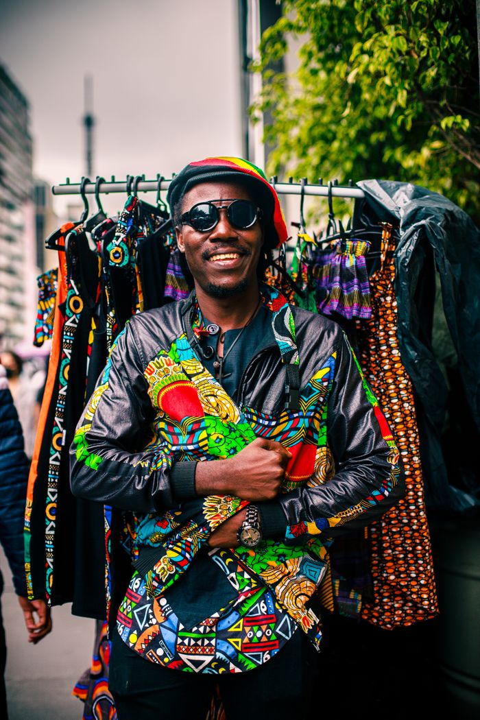 Smiling man in vibrant African clothing at a city market, showcasing unique fashion.