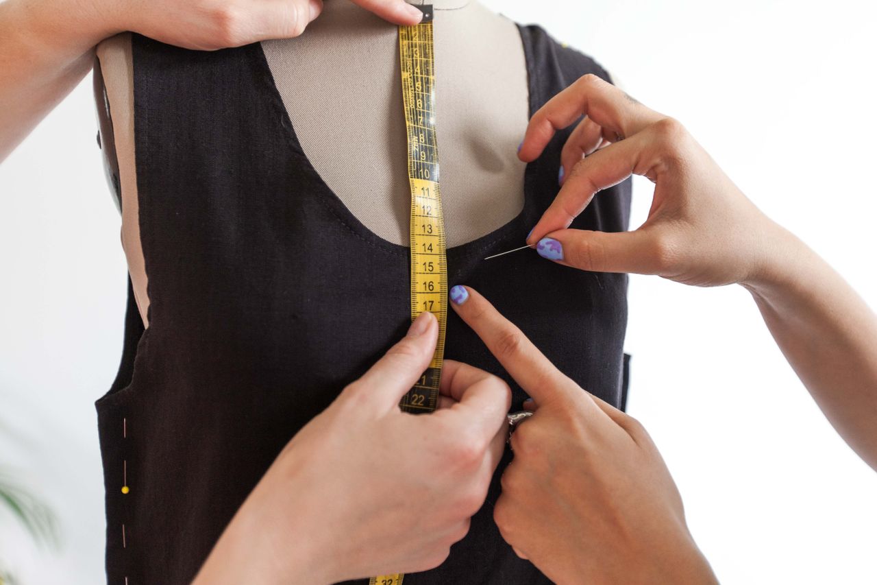 Close-up of hands measuring a dress on a mannequin, showcasing the fashion design process.