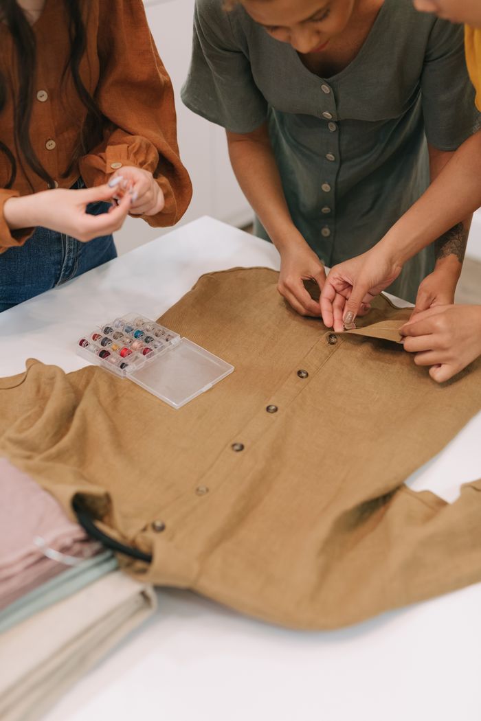 Fashion designers adjusting buttons on a brown shirt, showcasing teamwork and creativity in fashion design.